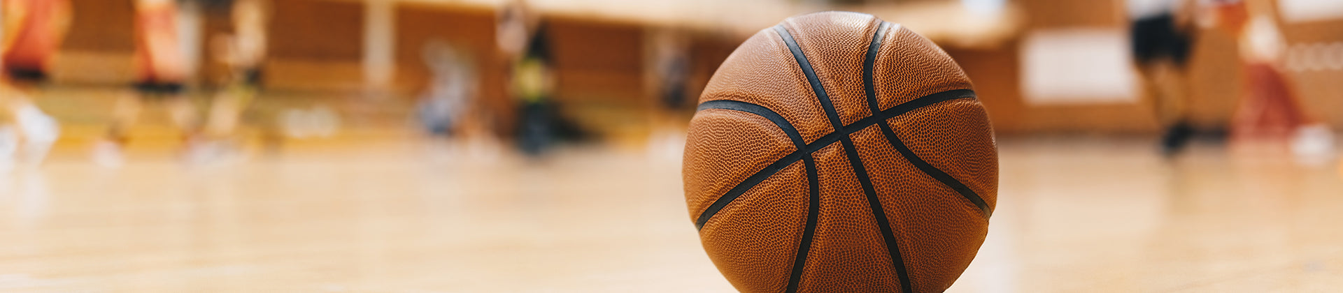 A close-up of a basketball on a polished indoor court, with blurred players and gym in the background.