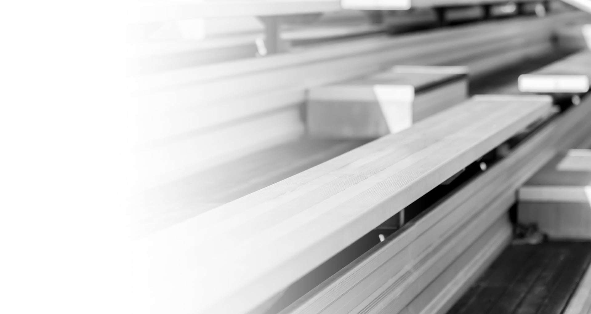 Black and white photo of empty wooden bleachers with a few scattered cardboard boxes placed on the seats; the left side of the image fades into white.