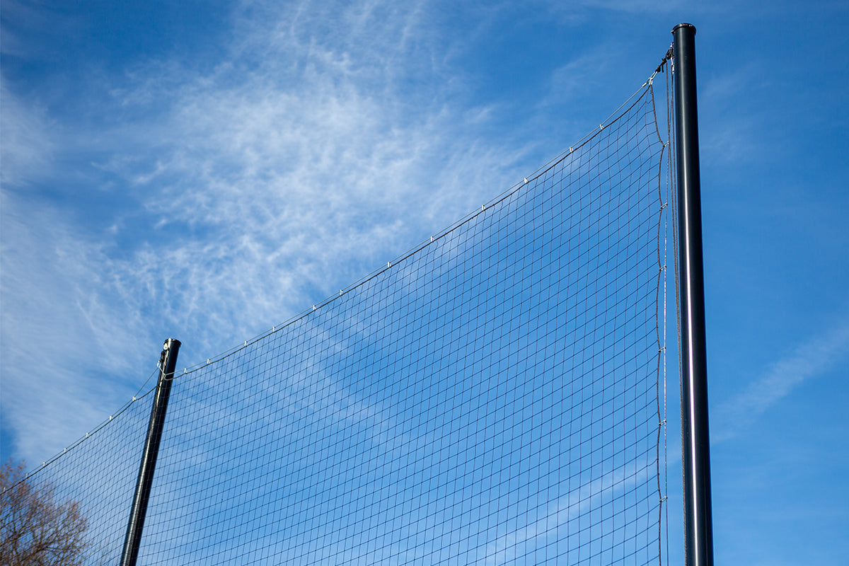 A close-up view of a volleyball net stretched between two poles against a bright blue sky with thin, wispy clouds.
