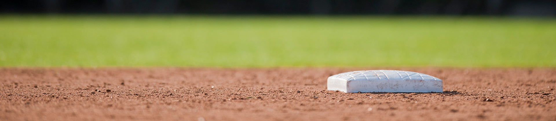 A close-up view of a baseball base on a dirt infield, with green grass in the background and no players visible.