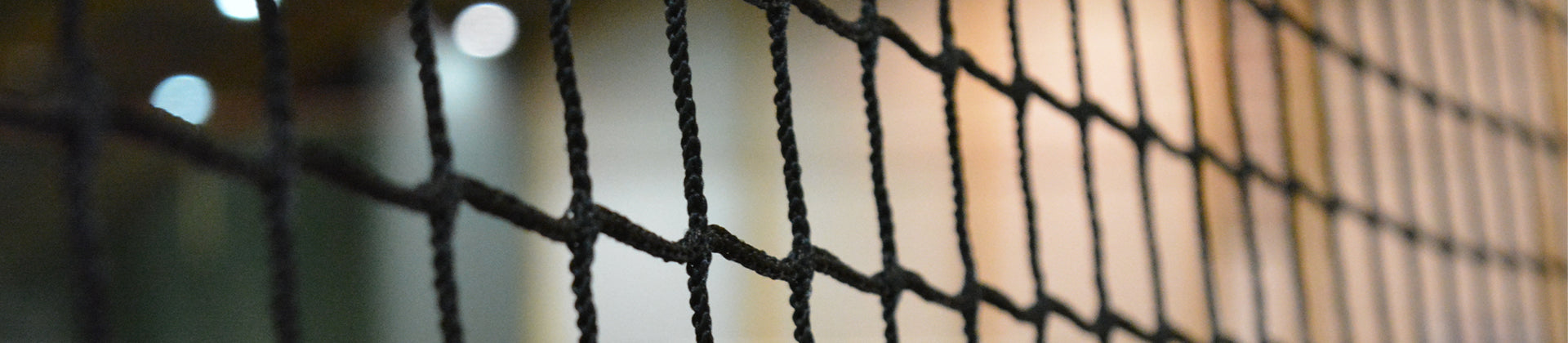 Close-up of a black net with a blurred background showing soft, out-of-focus lights and warm tones, highlighting the nets texture and pattern.