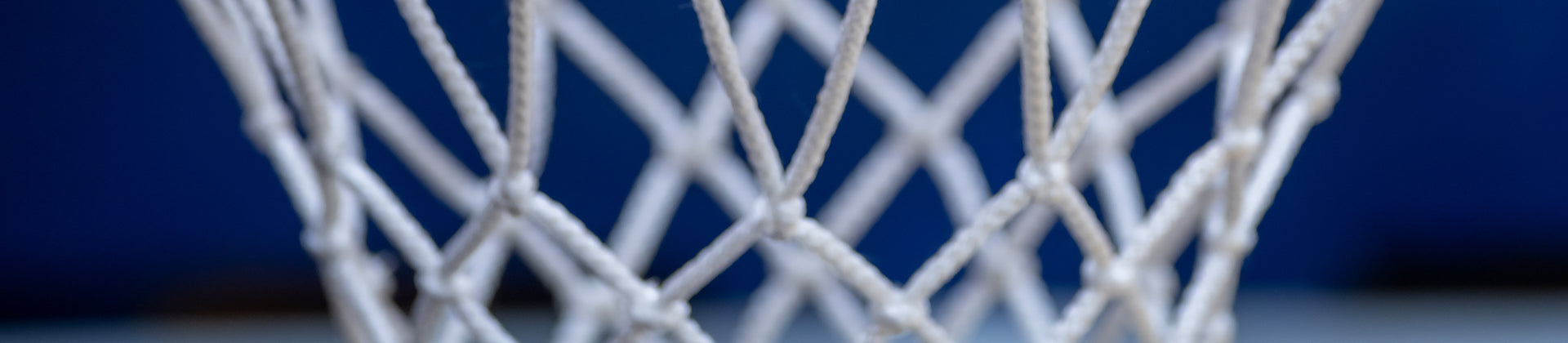 Close-up of a white basketball net with blue background, showing the braided strings and diamond-shaped pattern.