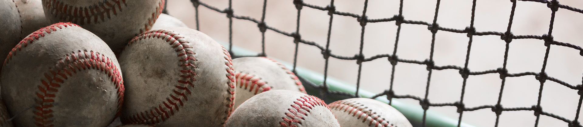 A close-up view of several worn baseballs stacked together next to a black net, with soft natural light illuminating the scene.