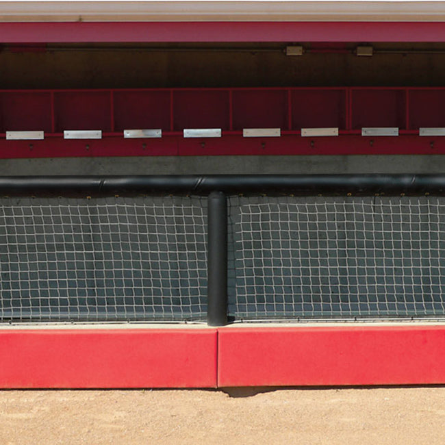 An empty baseball dugout features a Dugout Rail Padding Kit in custom colors, wire fencing, open cubbies, and a dirt floor in front.
