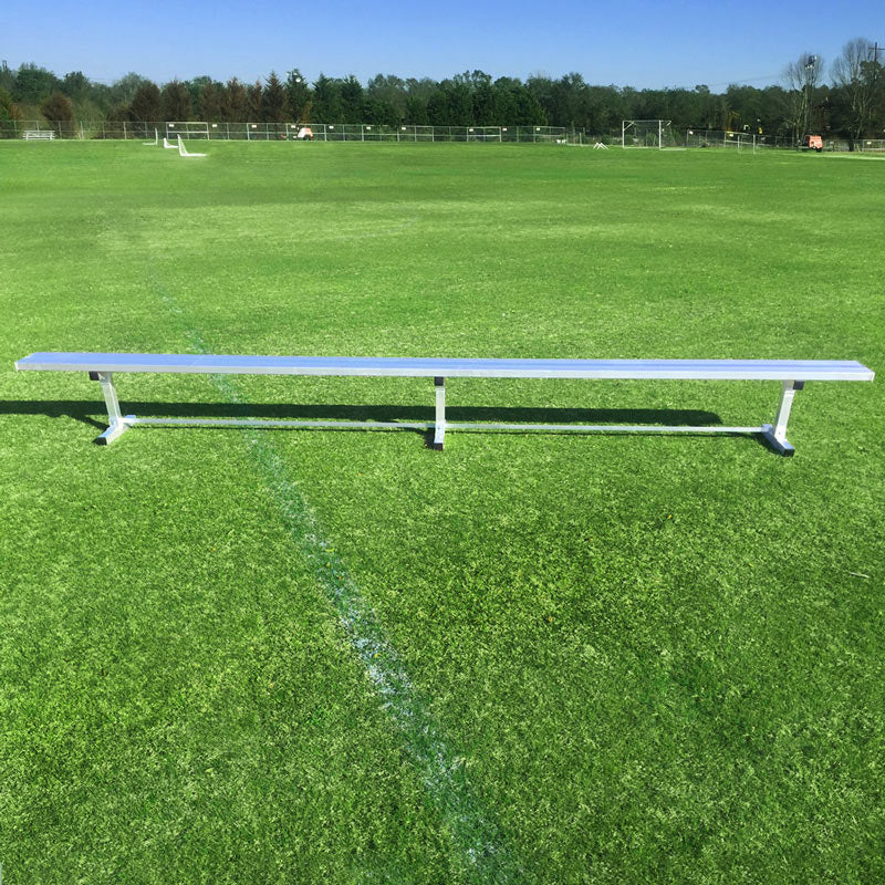 The Budget Portable Aluminum Team Bench, in silver, sits on green grass under a clear sky in an empty sports field, with goalposts visible in the background.