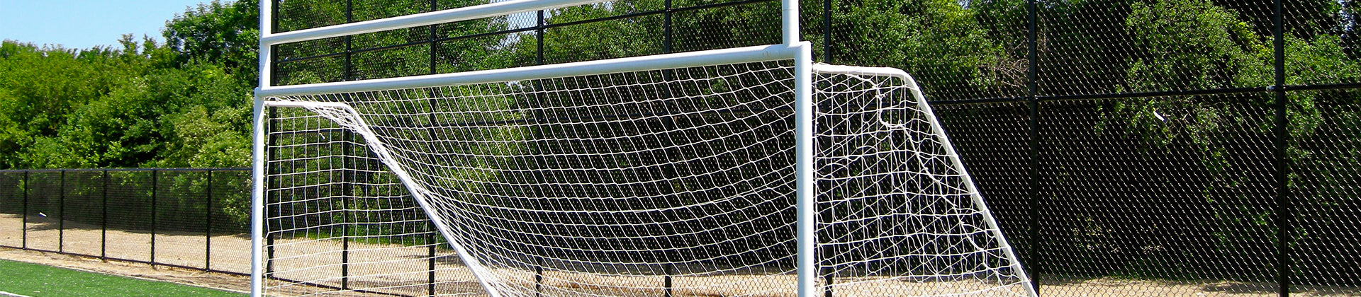 A combined soccer goal and football goalpost on a sports field, with a net attached and surrounded by trees and a black chain-link fence in the background.