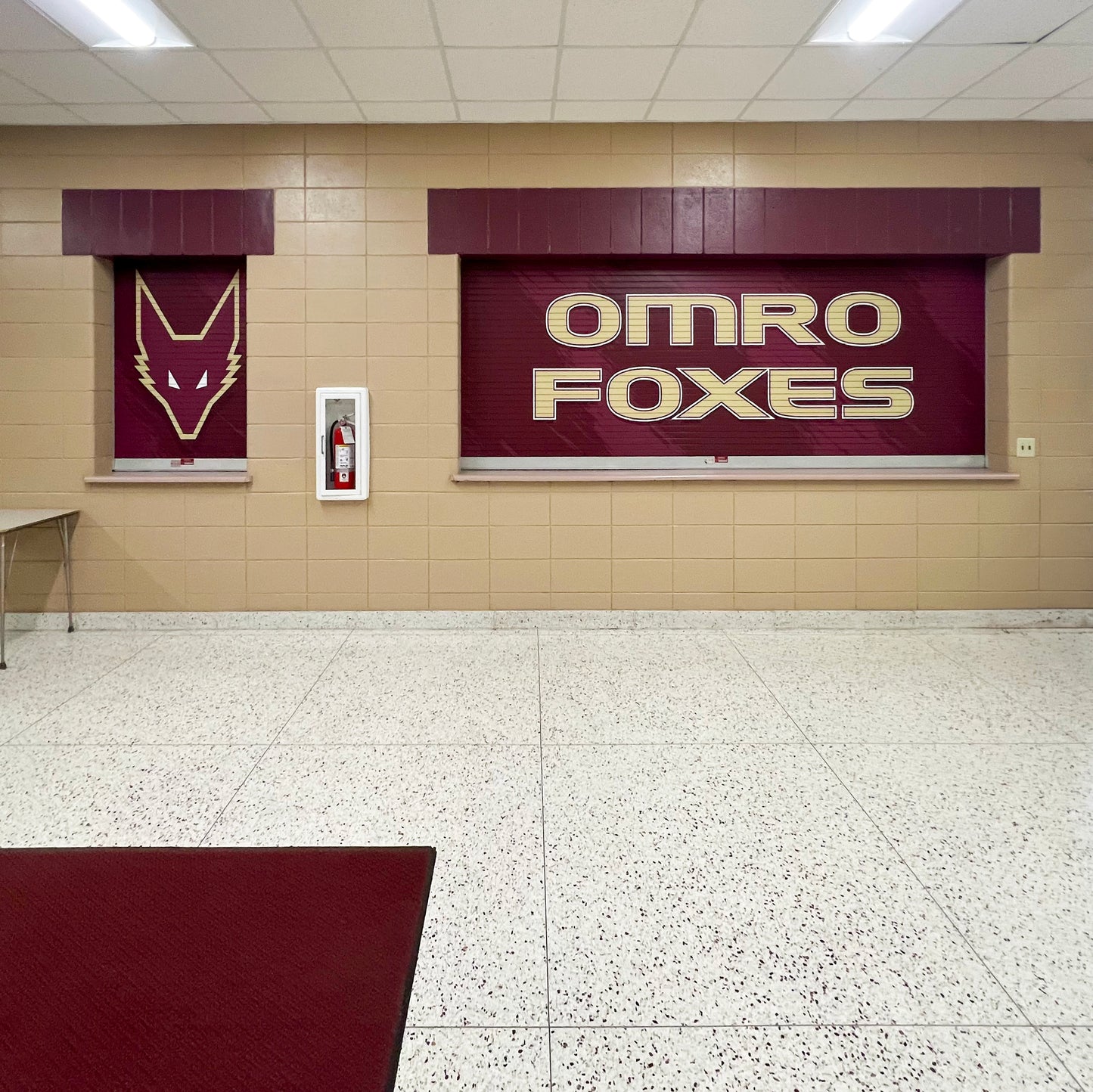 Maroon roll up concession stand doors with fox logo on left and Omro Foxes on right.