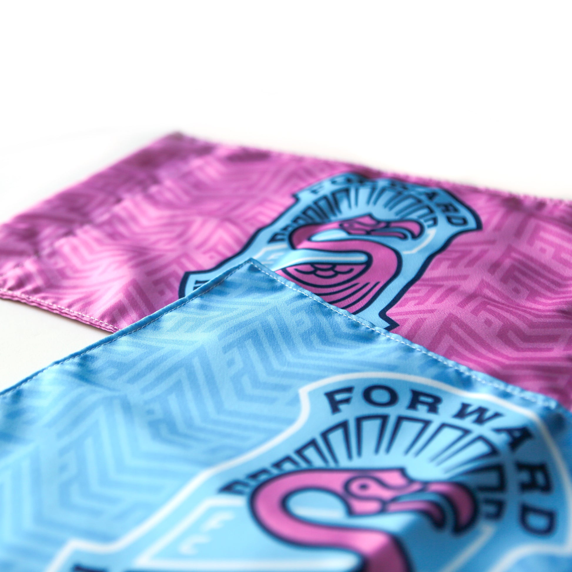 Close-up of Custom Soccer Corner Flags—one blue and one pink—both featuring a stylized flamingo and FORWARD with a bold S. The front blue flag highlights its unique patterned design, ideal for personalizing your soccer field.