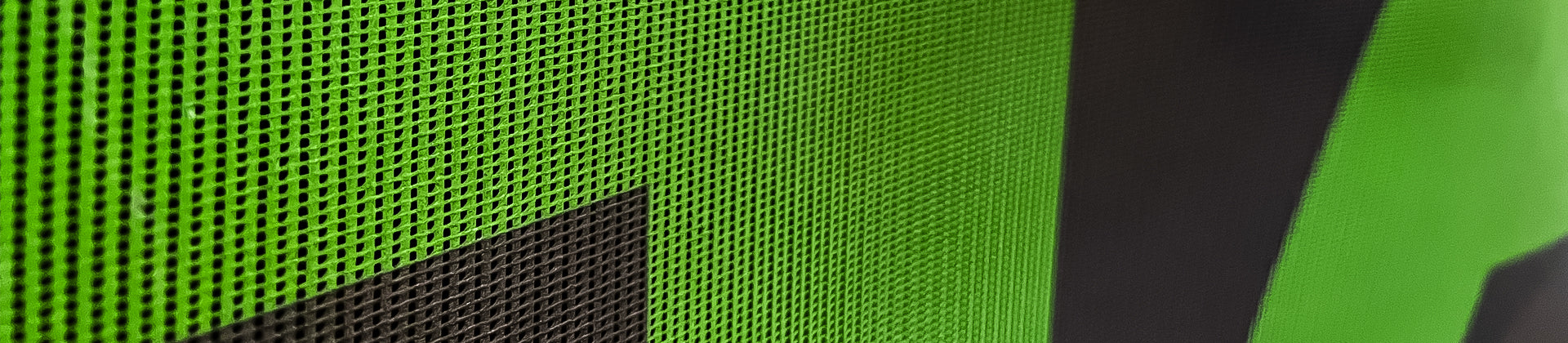 Close-up of a green perforated mesh surface with a large black geometric shape partially visible, creating a bold contrast and texture.