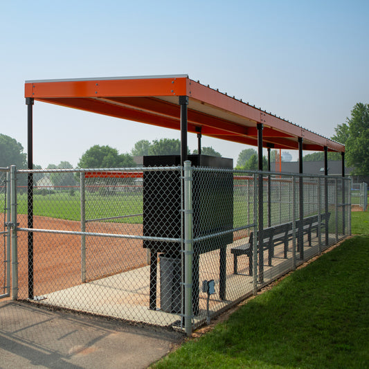 The World Series Dugout features a prefabricated steel roof and fencing, providing sun protection and shelter for players beside the field and diamond. Trees in the background add comfort and safety to this sturdy dugout.