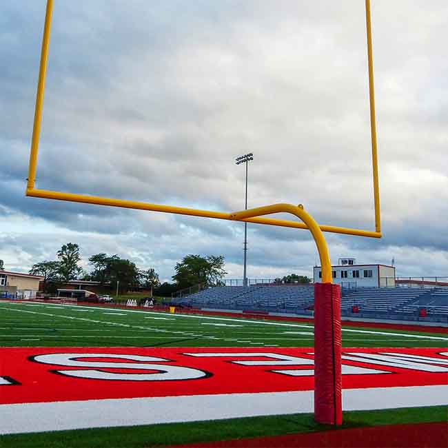Red padding around a football goalpost with a 6' overhang on a high school football field.