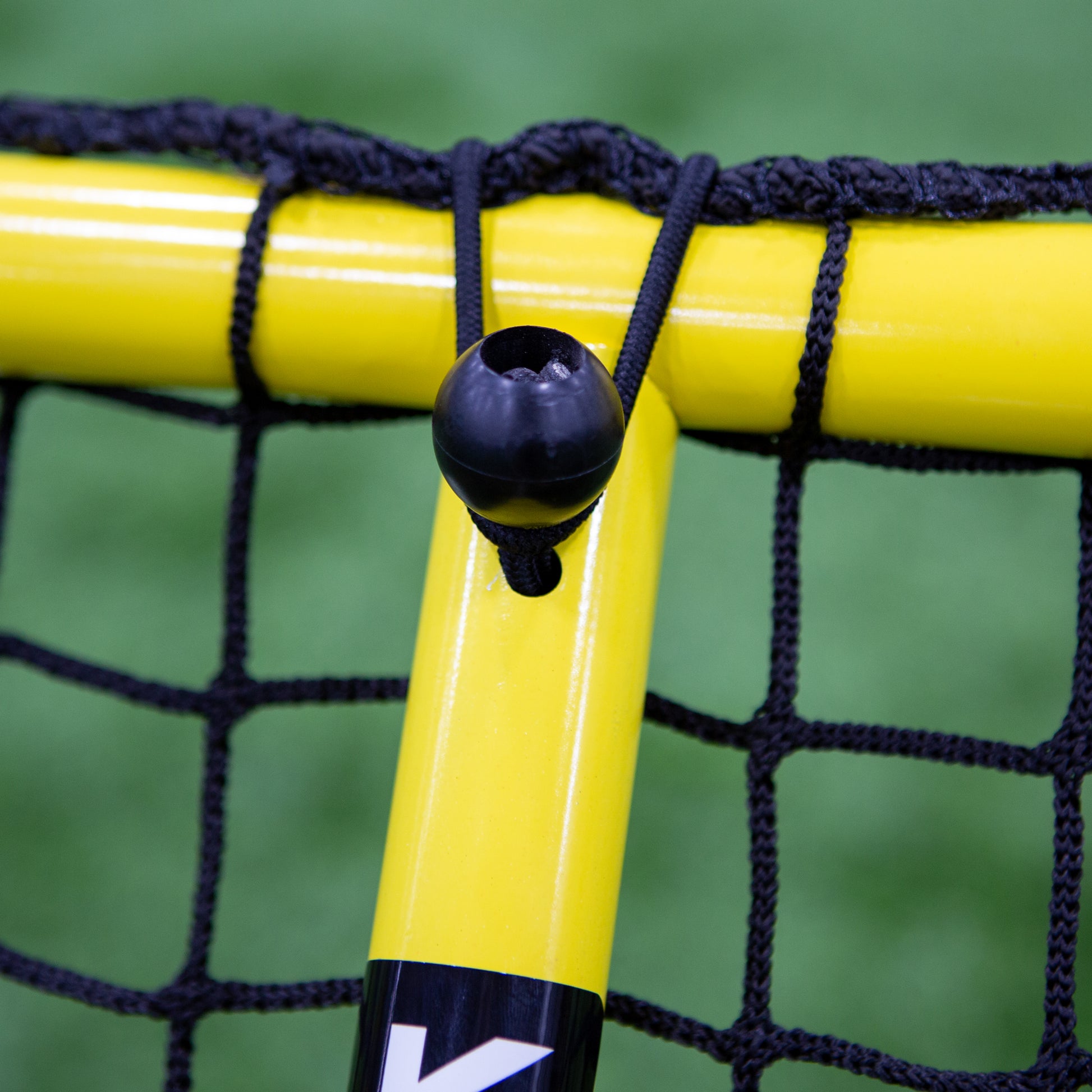 Close-up of a Folding Aluminum Soccer Goal with yellow frame and black netting. A black cord with a round stopper secures the net to the frame. Green turf appears in the background.