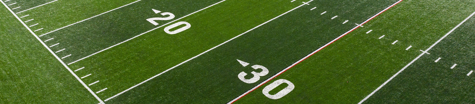 Aerial view of a football field showing white yard lines and numbers 20 and 30 on green artificial turf, with a red line crossing near the 30-yard mark.