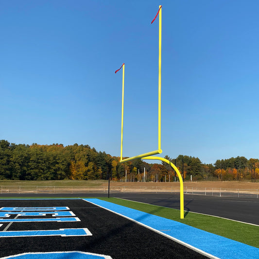Premium Football Goalposts with yellow aluminum uprights stand on a field featuring black, blue, and white end zone markings. Autumn trees and a clear blue sky form the backdrop.