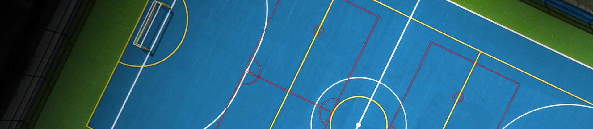Aerial view of a blue multi-sport court with various colored lines for different games, including soccer and basketball, surrounded by green artificial turf.