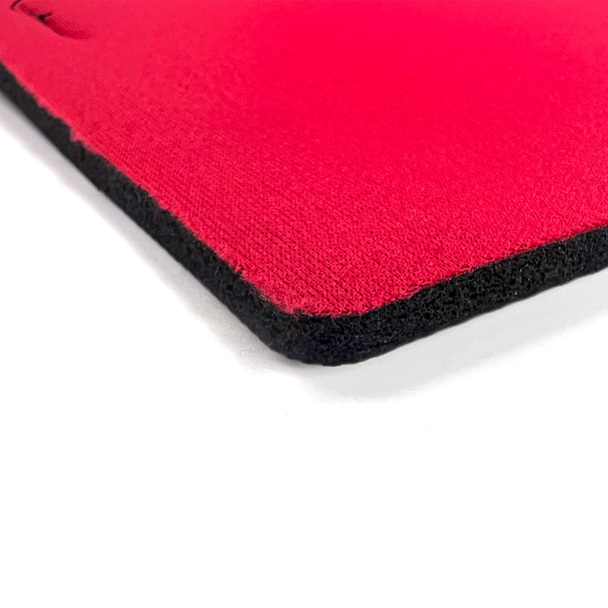 Close-up of the corner of a red rectangular mouse pad with a black textured edge and underside, resembling the Replacement Neoprene Pad (FFIT Soccer Goal For Grass), set against a white background.