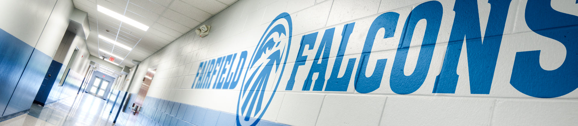 A school hallway with white and blue walls, featuring large blue letters on the right wall that read HOME OF THE FALCONS and a falcon logo. The corridor is brightly lit with ceiling lights.