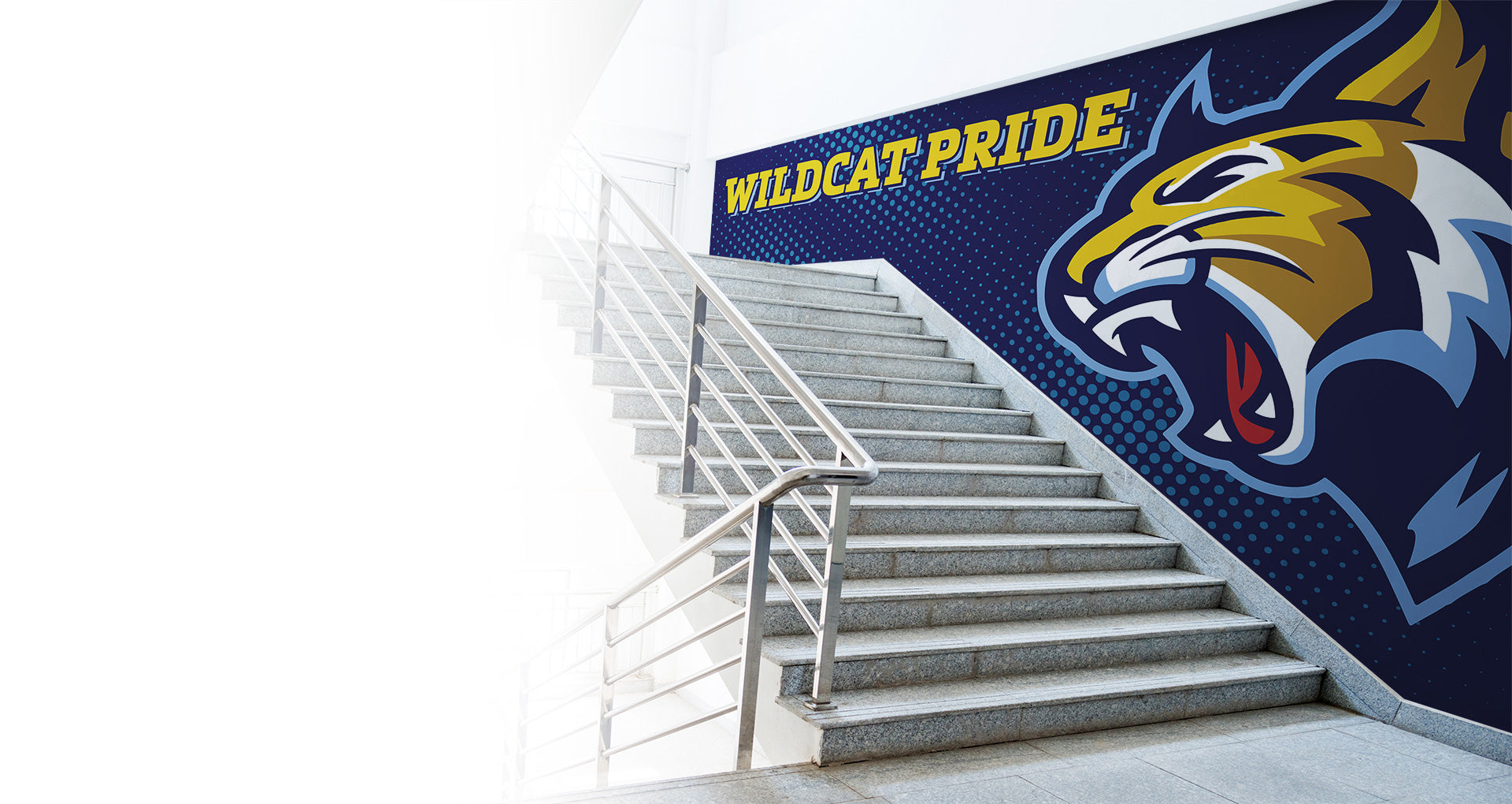 A staircase with metal railings beside a mural showing a roaring wildcat and the words WILDCAT PRIDE in bold yellow letters on a blue dotted background.