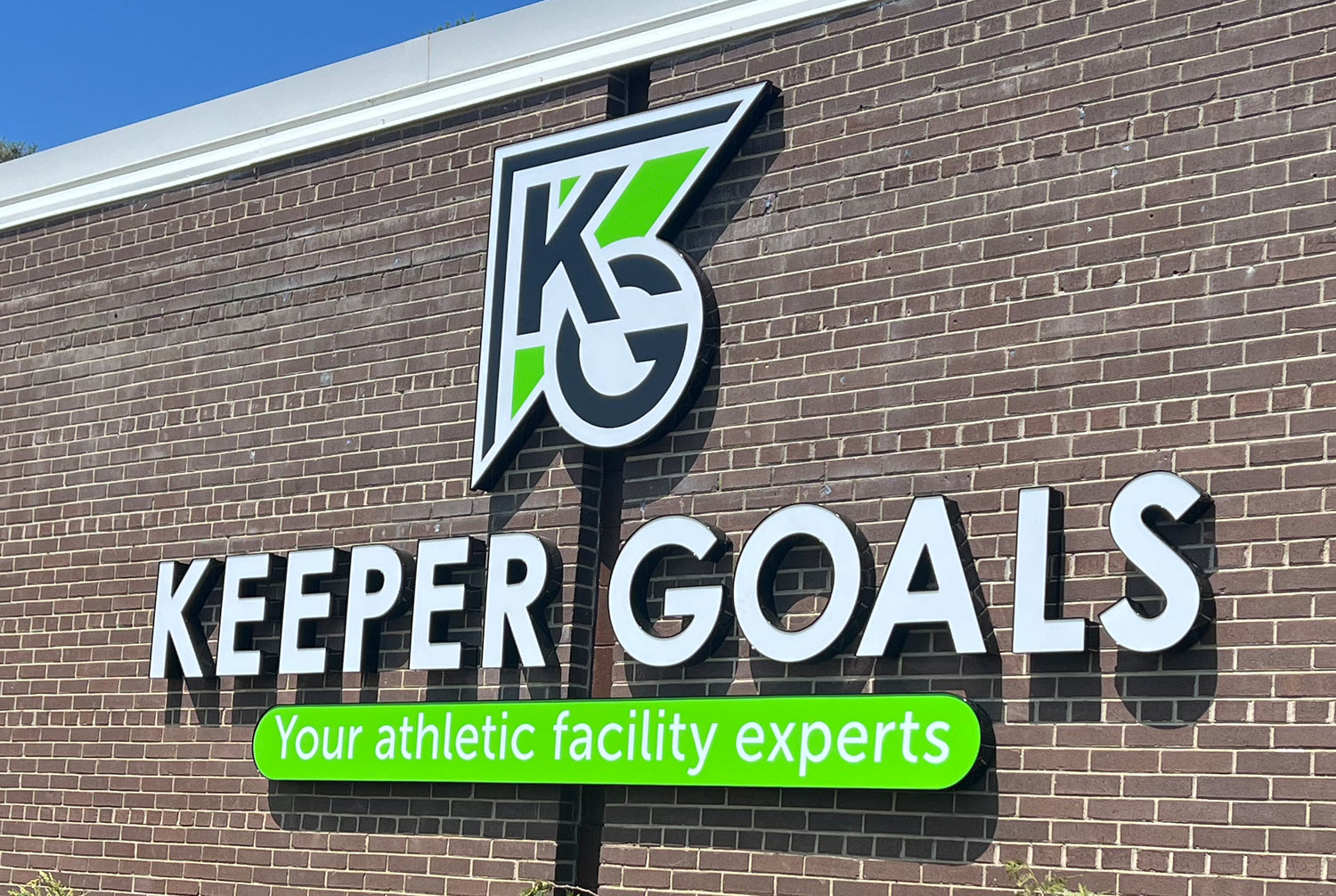 A brick building with a large sign that reads KEEPER GOALS and a logo with the letters KG above it. Below, a green banner says, Your athletic facility experts.