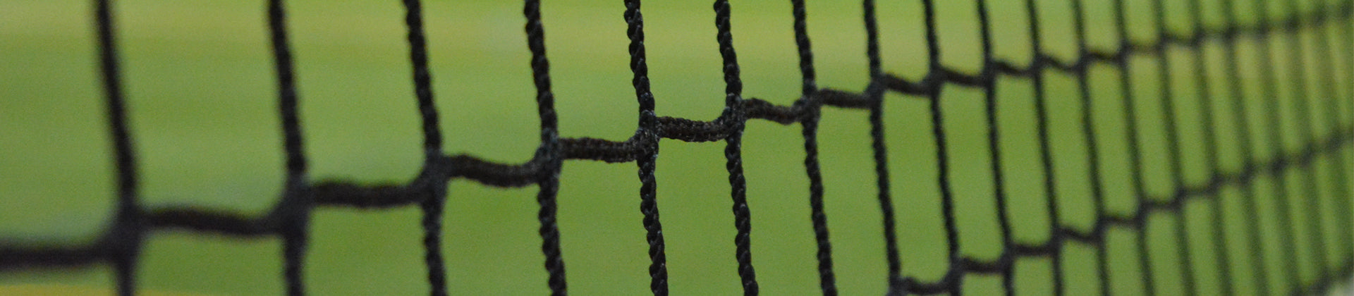Close-up of a black sports net, likely for tennis or volleyball, with a blurred green background suggesting a grass or outdoor court.