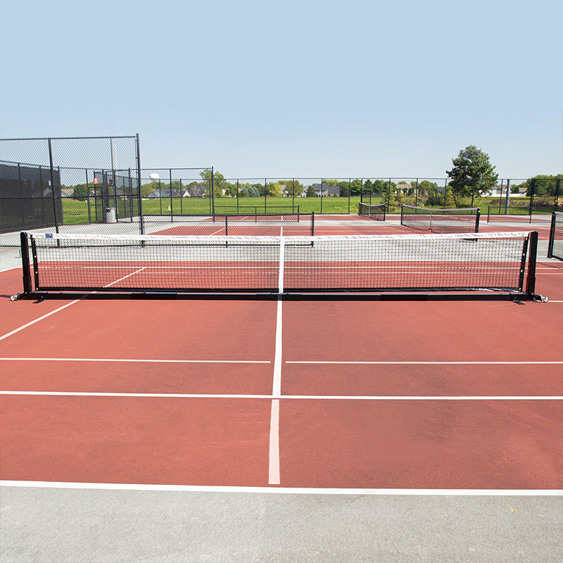Entire portable pickleball net on pickleball court with other pickleball courts in the background.