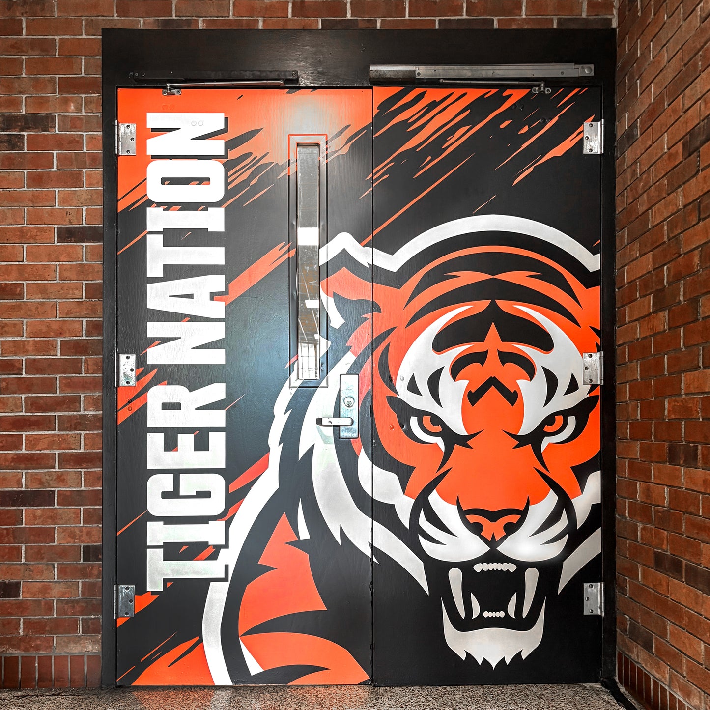 Custom Vinyl Door Wraps showcase bold school graphics with a striking orange, black, and white tiger face. "TIGER NATION" runs vertically on the left door, all set against a brick wall for maximum impact.