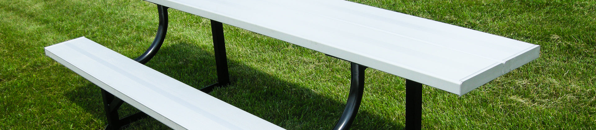 A white rectangular picnic table with attached benches and black metal legs sits on a green grass lawn.