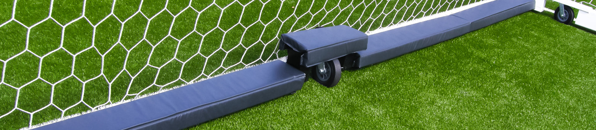 Soccer goal net and padded base on artificial grass, with a close-up of a protective wheel cover attached to the goal frame.