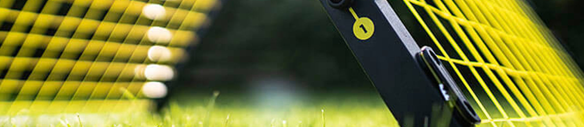 Close-up of a yellow wire fence angled into grass, with blurred sections of the fence in the background and a black post supporting the structure.
