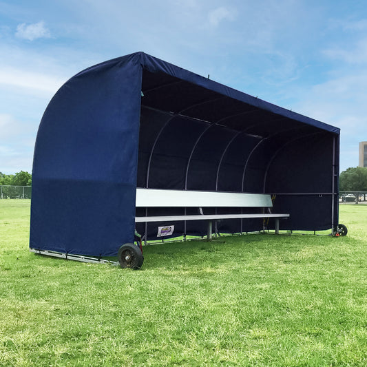 An Economy Team Shelter with a blue bench cover sits on grass under a blue sky. This wheeled shelter offers shaded sideline seating and protection for soccer teams or groups.