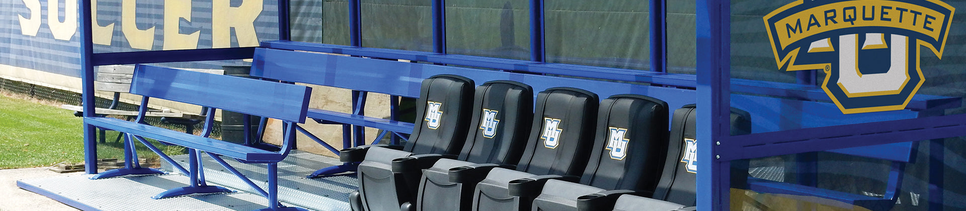 Blue metal team benches with black seats featuring the Marquette University logo, under a blue shelter by a sports field. The Marquette MU logo is prominently displayed on the side panel.