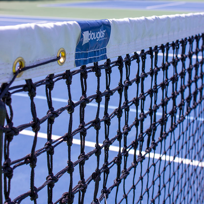 Close-up of the TN-36DMT Double Mesh Tapered Tennis Net, official size and black braided polyethylene with white band and Douglas label, set on a blue court with white lines in the background.