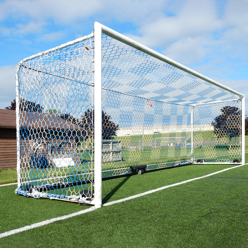 The Ultimate Wheeled Box-Style Soccer Goal with a net stands on green artificial turf under a blue sky with scattered clouds, while a building and trees appear in the background.