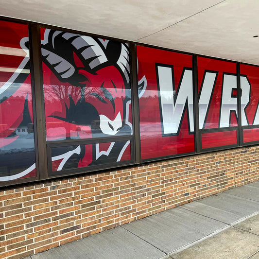 A building window displays an angry red ram mascot and white WRA letters on a red background using Perforated Window Film, providing striking branding and enhanced privacy.