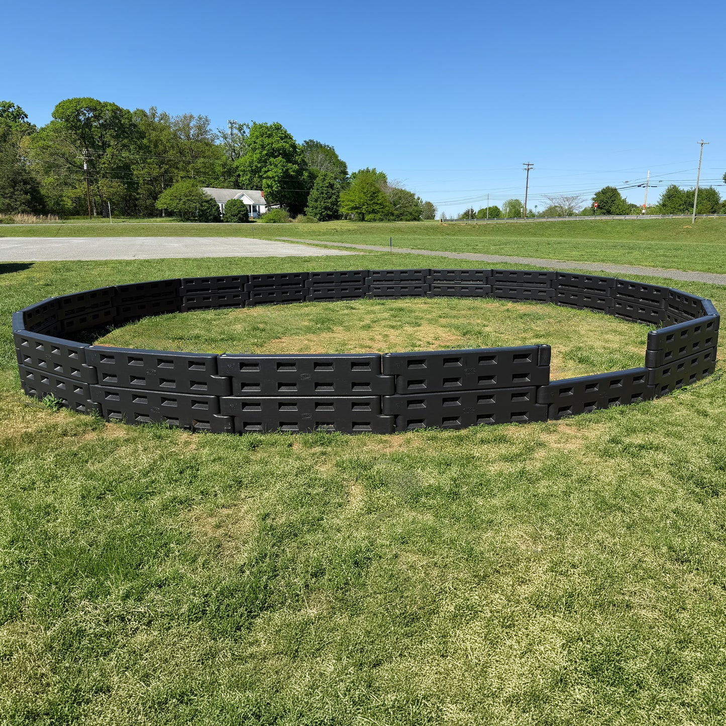 An APS Standard GaGa Ball Pit | Permanent In-Ground Mount stands on a grassy field beneath a blue sky, creating an ideal outdoor playground with trees and a road visible in the background.