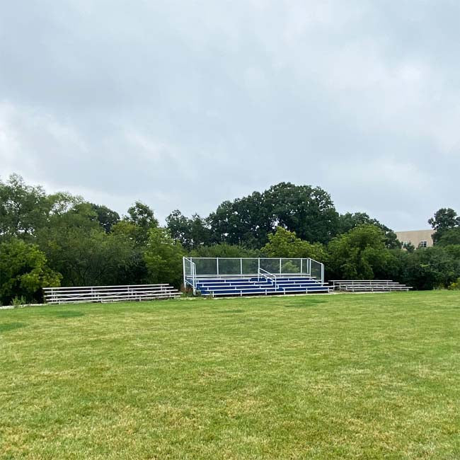 Model #B5R31A1GR. 5 row 31' bleachers with blue risers at a soccer field.