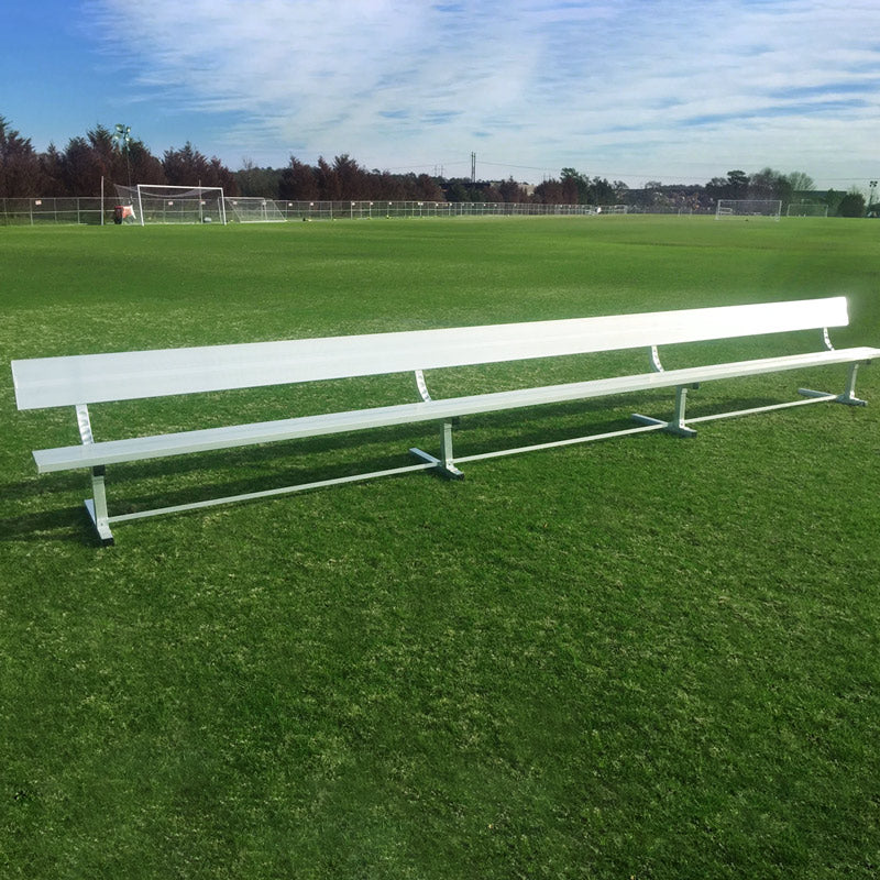 The Budget Portable Aluminum Team Bench (With Backrest) stands on a lush green soccer field under partly cloudy skies, with goals and trees in the distance.