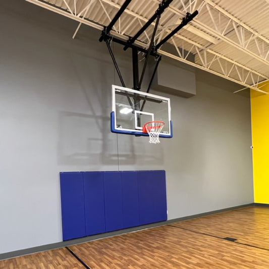 Ceiling mounted basketball hoop in rec center gym. Blue padding on gray wall behind the hoop.
