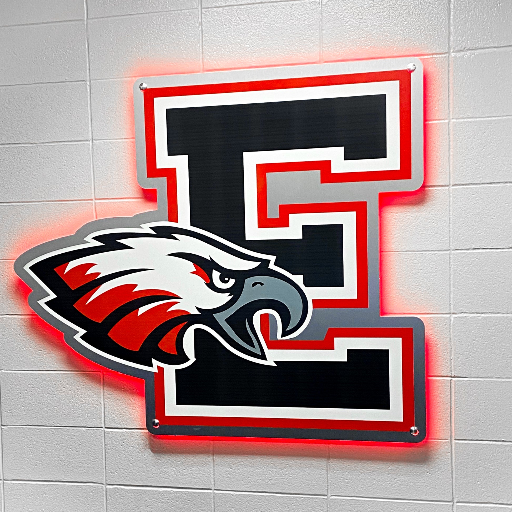 A 3D Signage or Lettering piece featuring a large black letter E outlined in red and white with a red, white, and black illustrated eagle head overlapping, custom mounted on a white tiled wall.