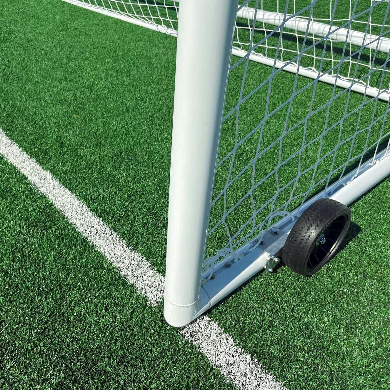 Close-up of the Elite Stadium Soccer Goals on artificial green turf by a white corner line, featuring a black wheel for easy movement and durable aluminum stanchion poles.