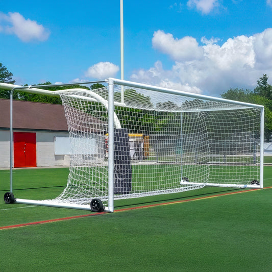 An Elite Box-Style Soccer Goal with a net sits on green artificial turf. This portable soccer goal has wheels for easy movement, with buildings and a blue sky with clouds visible in the background.