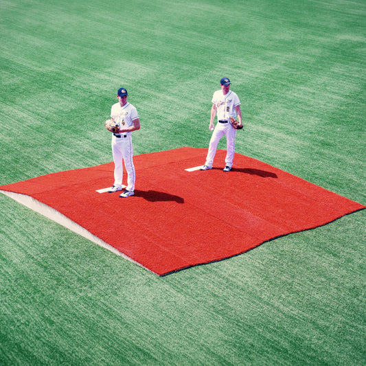 Two baseball players in white uniforms stand on adjacent The Perfect Mound Portable Bullpen Pitching Mound Series on a green field, each holding a glove and ball, facing forward.