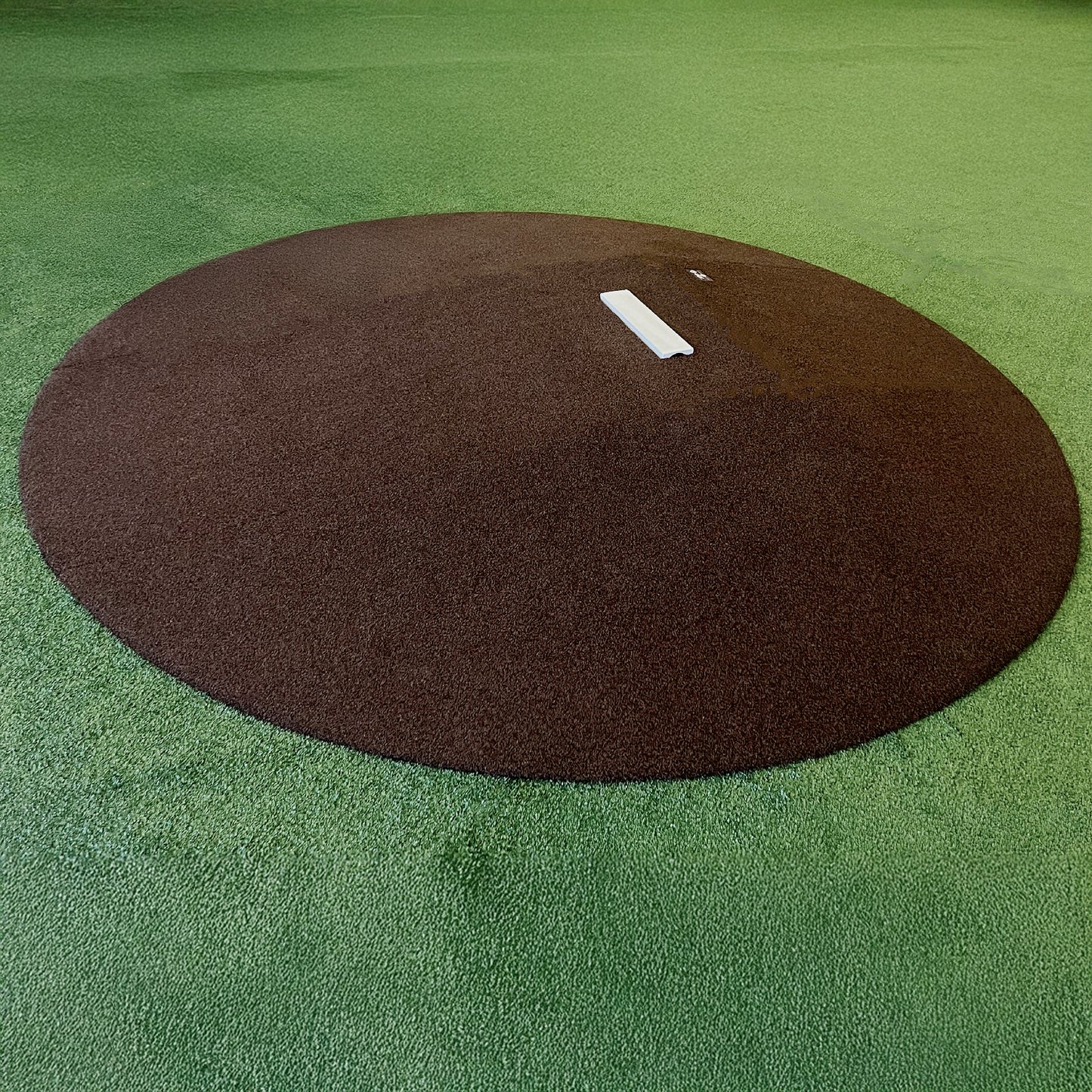 The Perfect Mound Youth Portable Pitching Mound, a brown circular mound with a white pitching rubber, is ideal for Little League and youth baseball on green artificial turf fields.