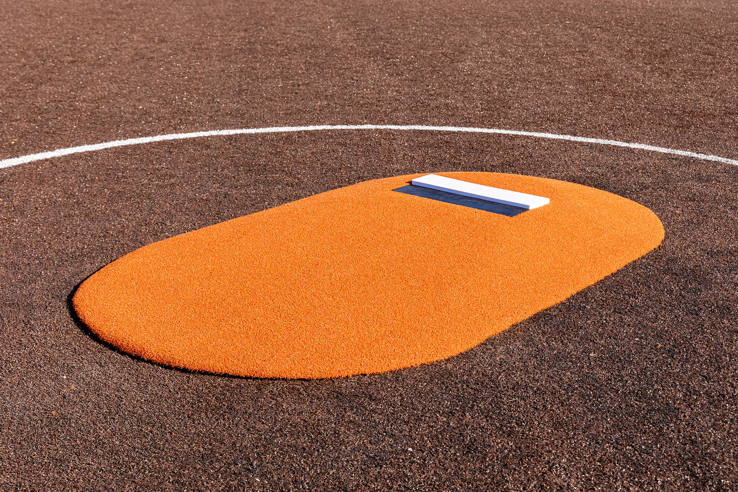 The Portolite 6″ One-Piece Game Mound, designed for ages 8-13, features an orange surface with a white pitcher’s rubber and is pictured on a brown baseball field partially outlined by a white curved line—making it ideal for Little League tournament play.