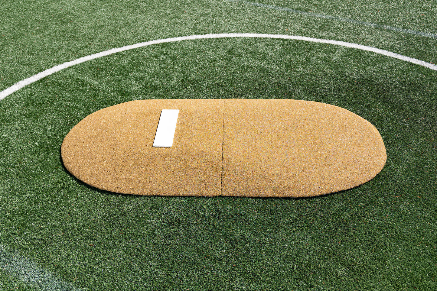 The Portolite 6″ Two-Piece Game Mound for ages 9-13 features a tan oval mound with a white rubber plate, set on green artificial turf and outlined by a white circular boundary—ideal for tournament play as a portable game mound.