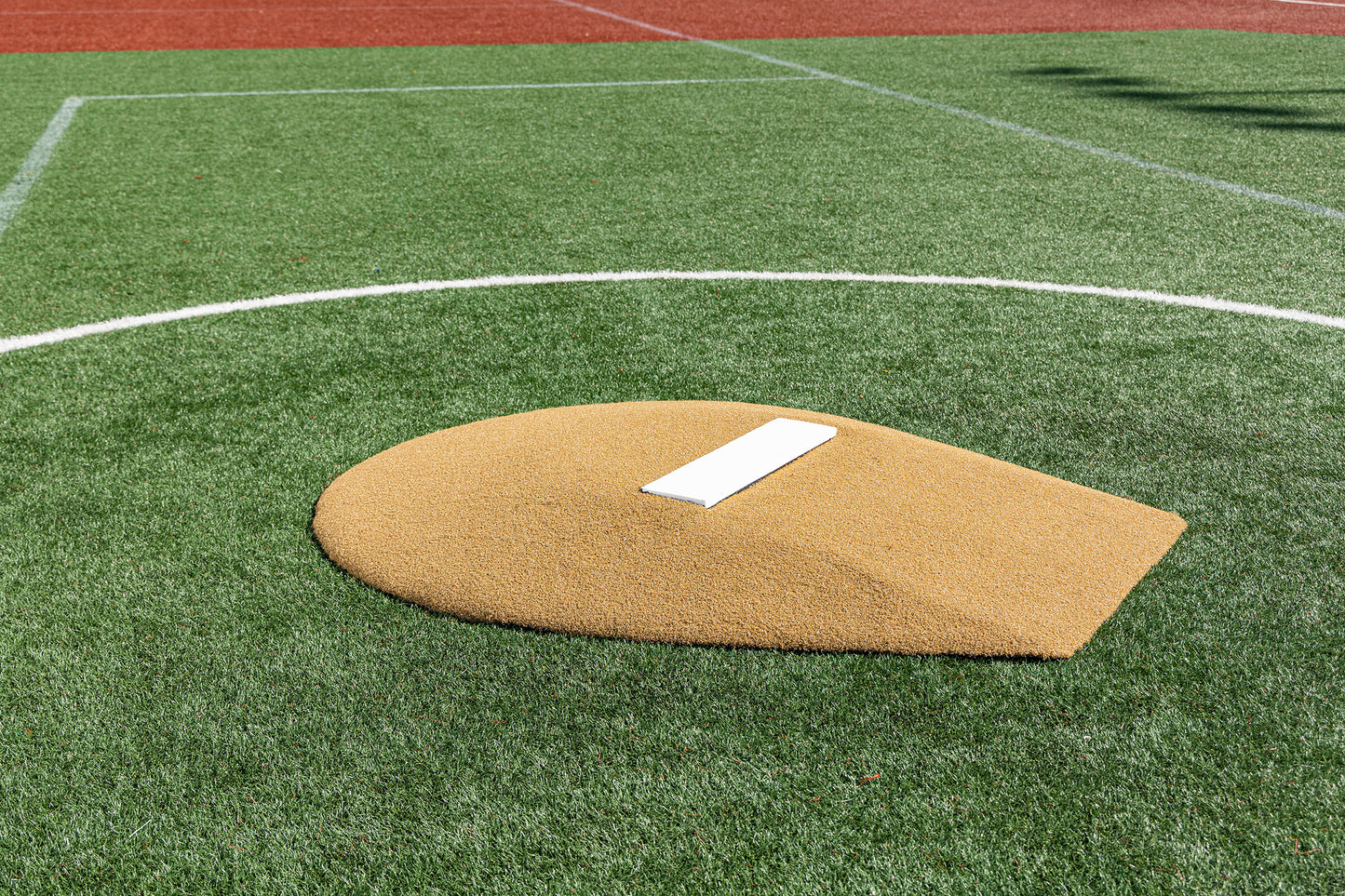 The Portolite 6″ Stride Off Game Mound, designed for ages 13 and under, features a white rubber pitching plate set on artificial turf, surrounded by green and red surfaces with sports field markings—making it ideal for youth pitchers preparing for their next Little League game.