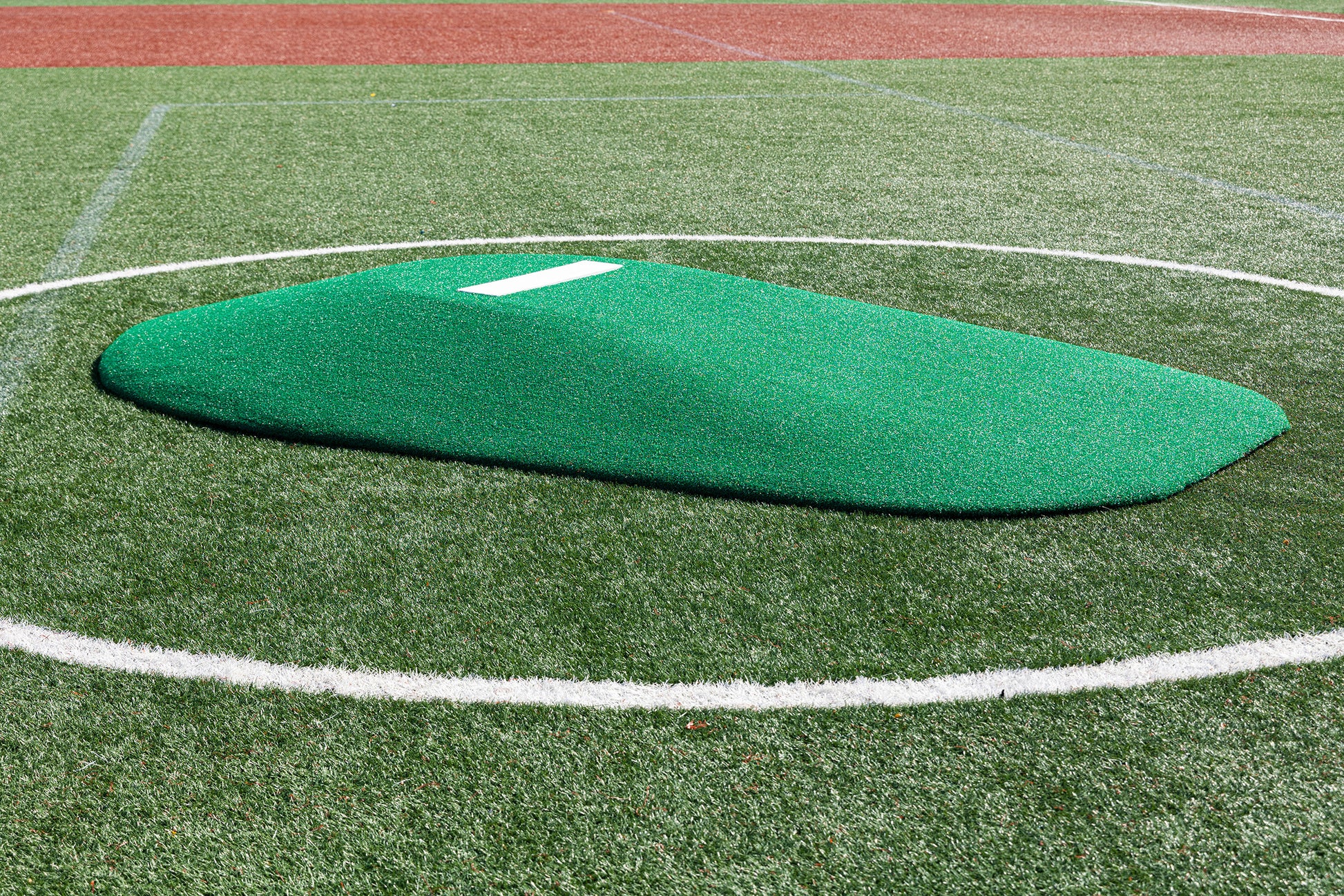 A Portolite 8″ One-Piece Game Mound for ages 13-15 sits inside a white circle on a baseball field with artificial turf, making it perfect for Babe Ruth level play and multi-age tournaments.