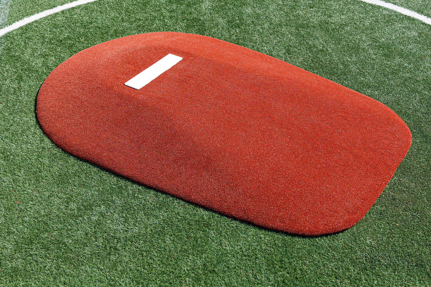 The Portolite 10″ One-Piece Game Mound, a heavy-duty regulation pitching mound in red with a white rubber plate, is set on green synthetic turf inside a white circular line—perfect for high school baseball practices or games.