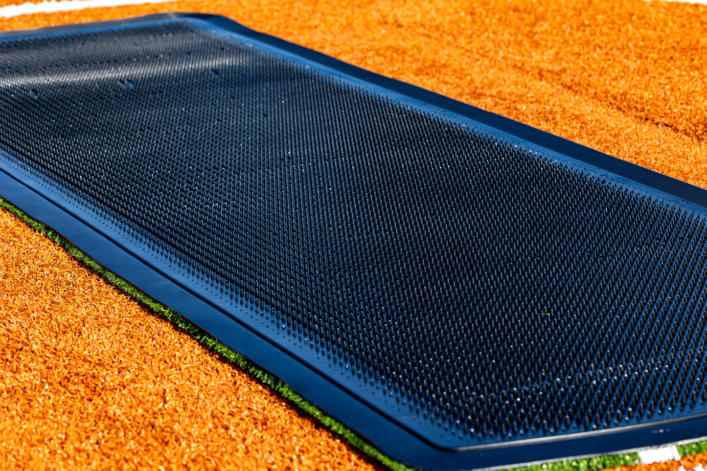 A 13′ x 4′ Portolite Pitching Mound Protector is laid into the ground, bordered by orange rubber mulch and a slim strip of artificial grass for enhanced turf protection.