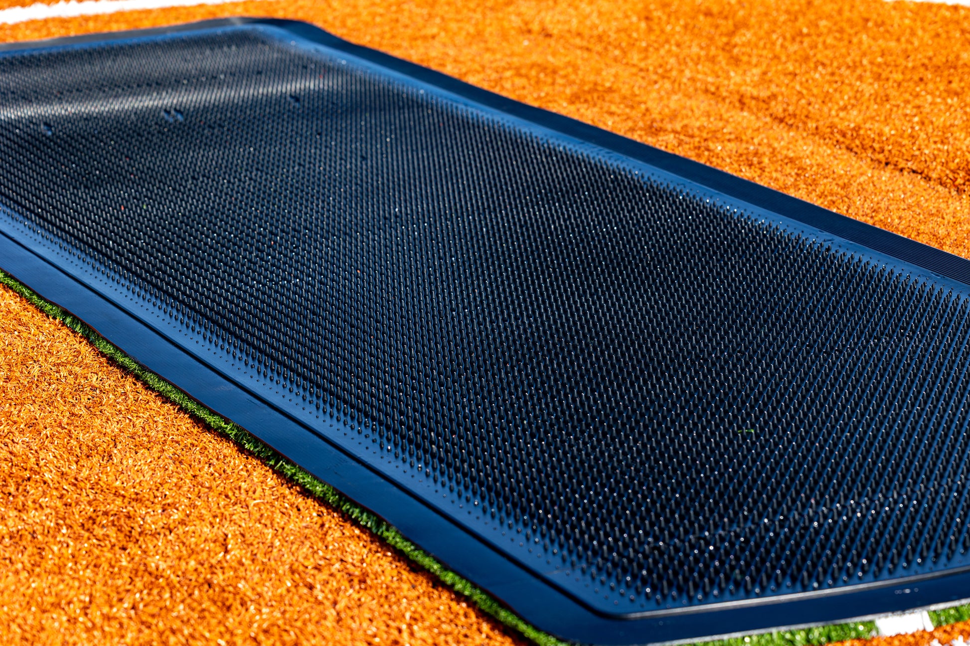 A 13′ x 4′ Portolite Pitching Mound Protector is laid into the ground, bordered by orange rubber mulch and a slim strip of artificial grass for enhanced turf protection.
